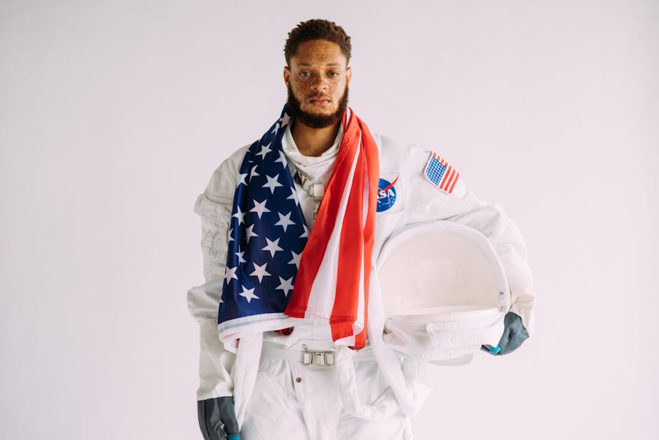 NASA Artemis II Görevinde Astronotlar İçin Özel Mobil İletişim Sistemi — Astronaut wearing a suit holding a helmet and draped in an American flag.